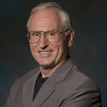 Elderly man smiling wearing a grey suit and glasses